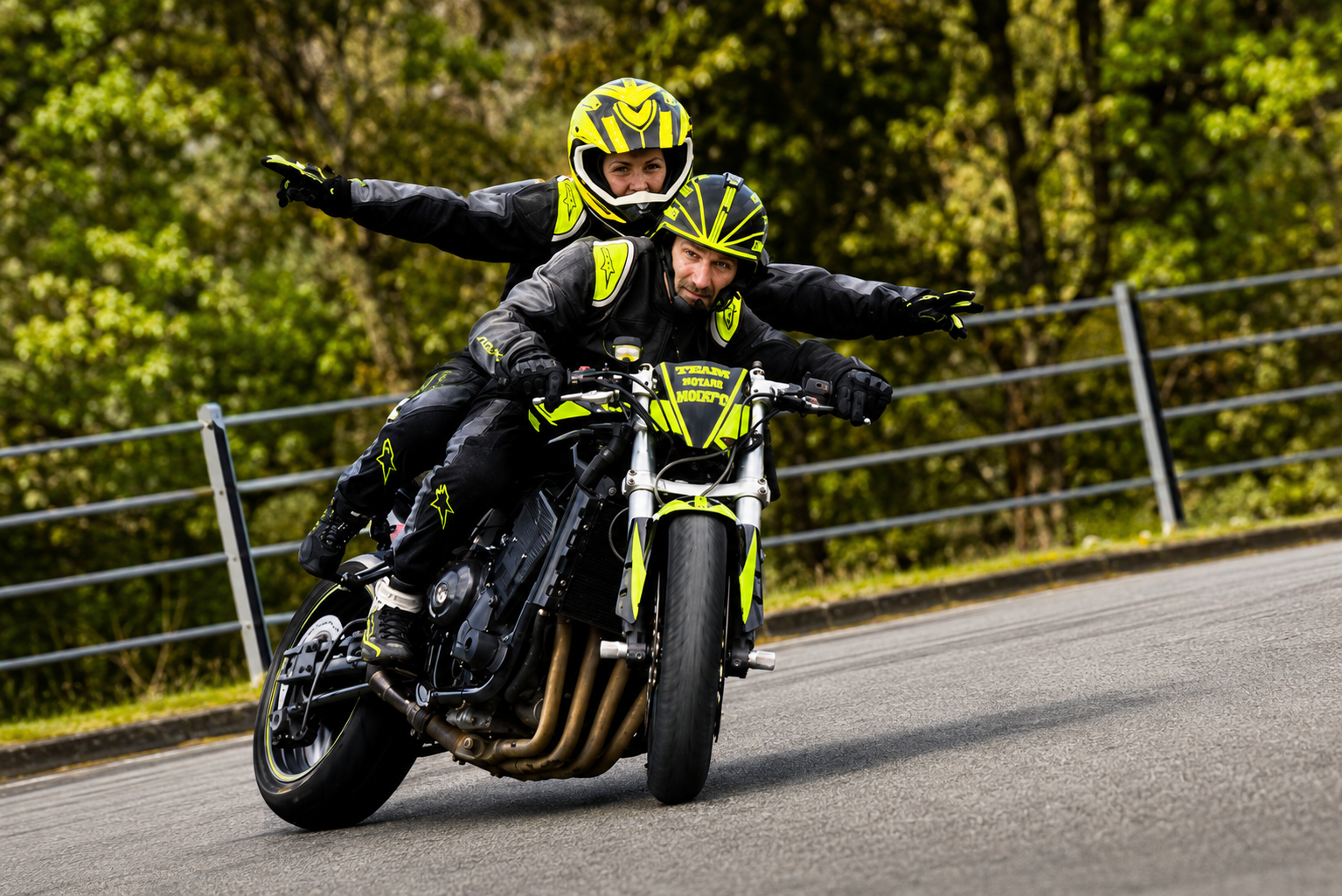 Moto en glisse à deux, la passagère bras écartés, livrée noir et lime.